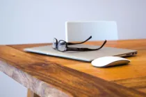 Ein Laptop mit Computermaus und eine Brille liegen auf einem Tisch